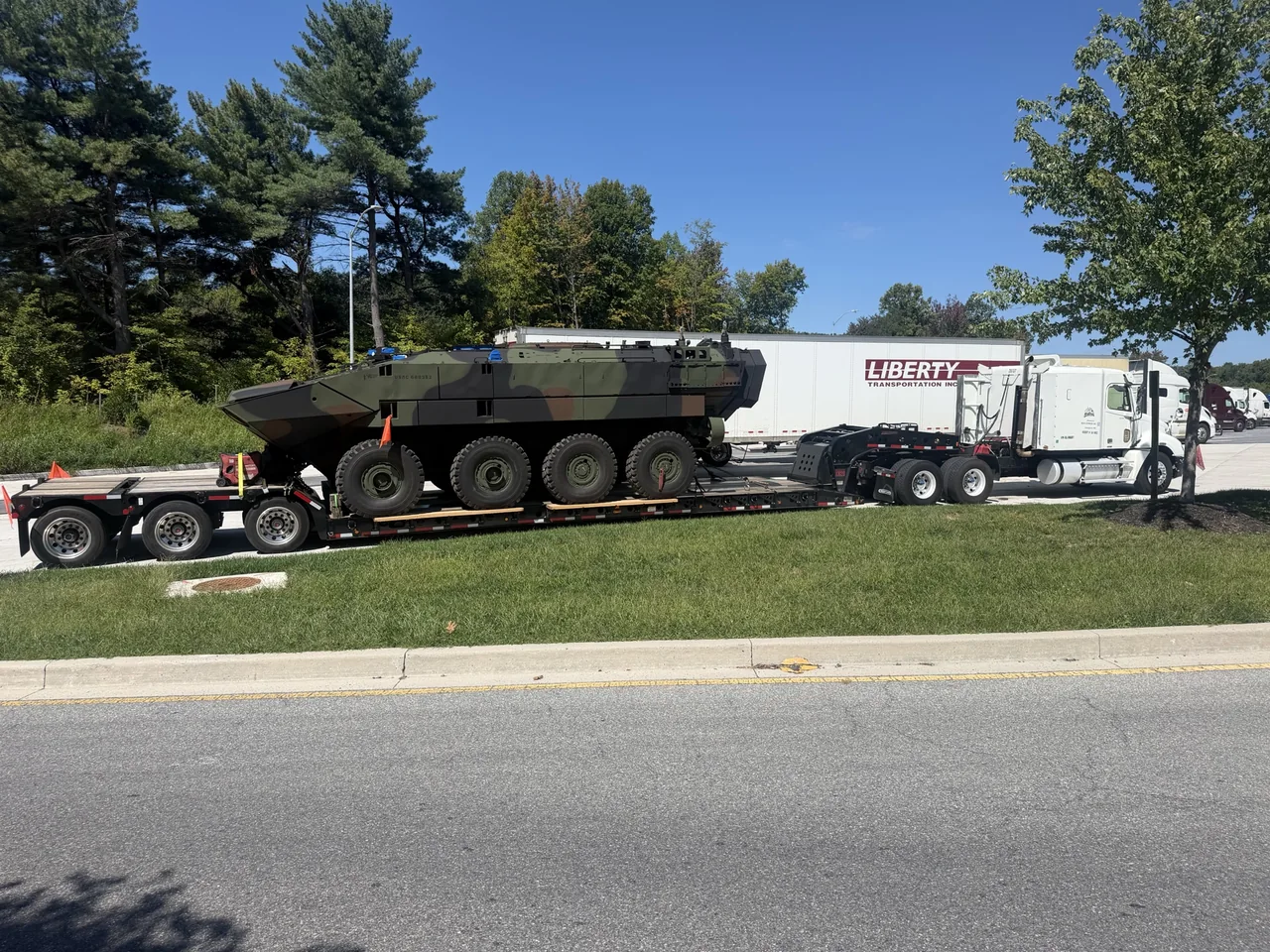 White truck and RGN lowboy trailer transporting a large eight-wheel heavy vehicle
